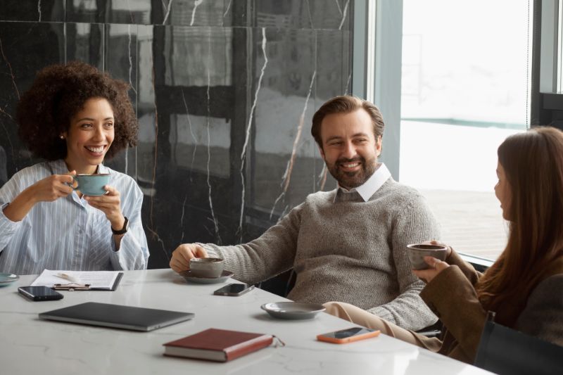 Corretores em mesa de reuniões enquanto discutem propostas e tomam café com cliente