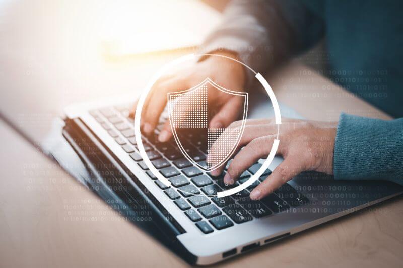 Homem mexendo em um notebook com a ilustração de um escudo por cima representando a proteção contra vazamento de dados